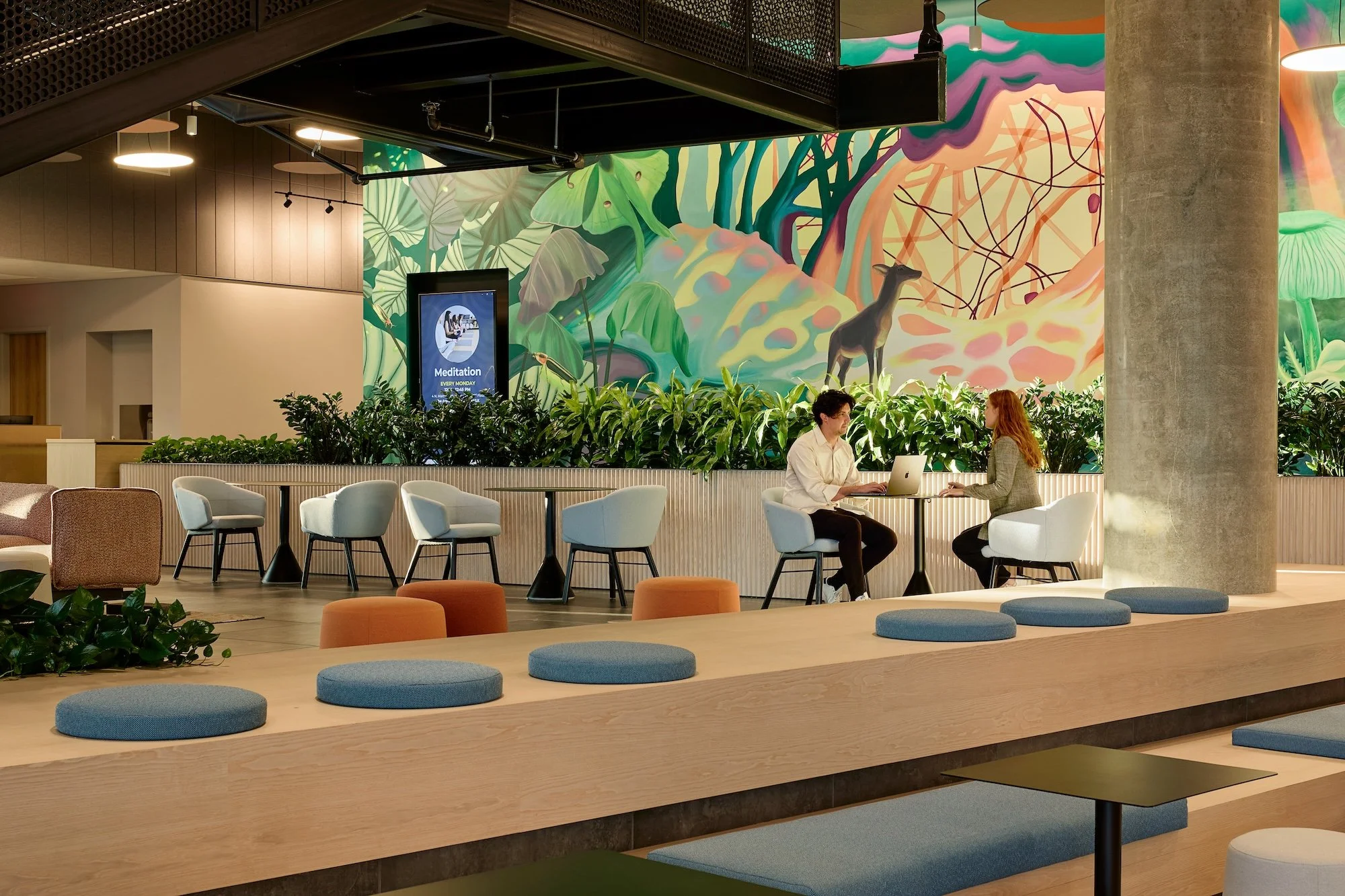 Tables and lounge seating beside a colorful mural at the Civic Lounge at 4MLK.