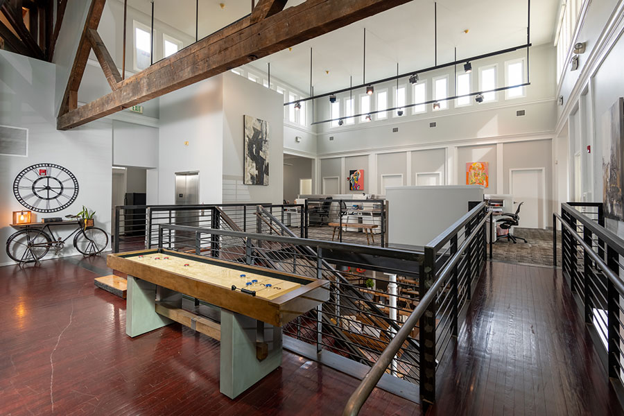 Shared desks beneath exposed wooden beams and a mezzanine at CO-BALT Workspace.